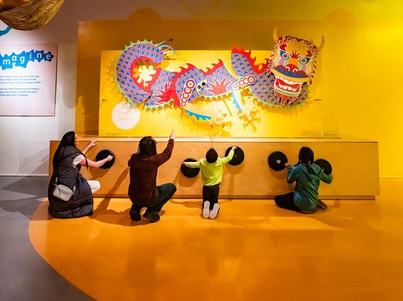 A family of four turning wheels to move a colourful dragon model on a wall above.