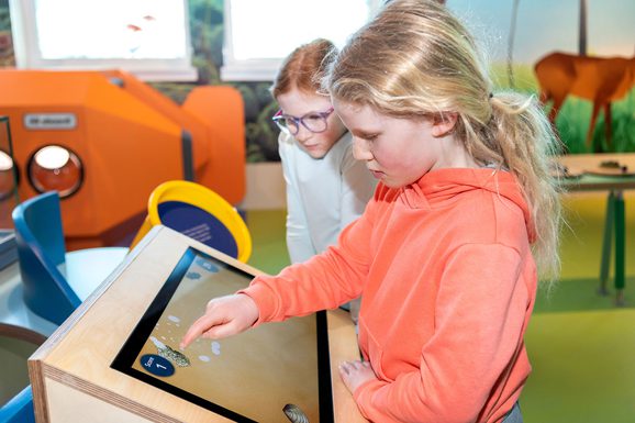 Two young girls play with an interactive screen in a colourful, playful space.