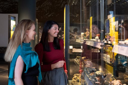 Two women looking at geological samples in a museum display case.