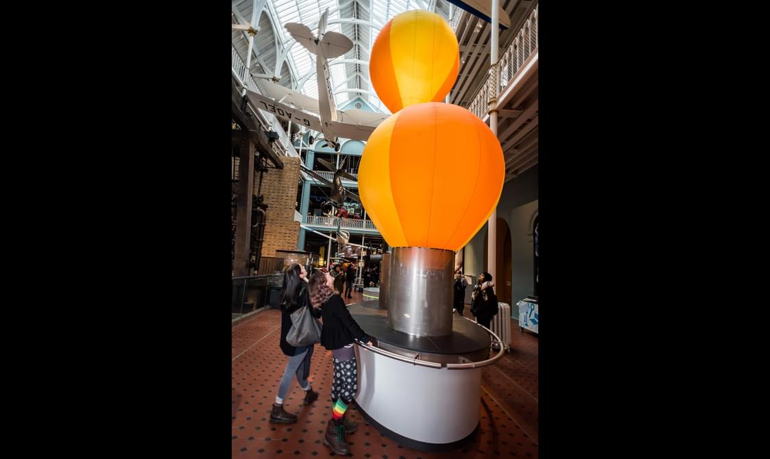 Two visitors watching hot air balloons ascend in a museum gallery.