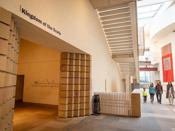A family walk towards a museum gallery entrance with a sign above that reads, "Kingdom of the Scots."