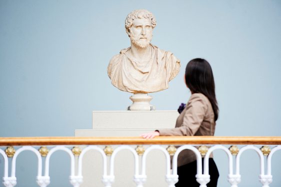 A visitor looks at a bust sculpture of a Roman figure.