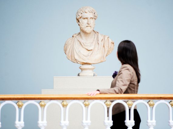 A visitor looks at a bust sculpture of a Roman figure.