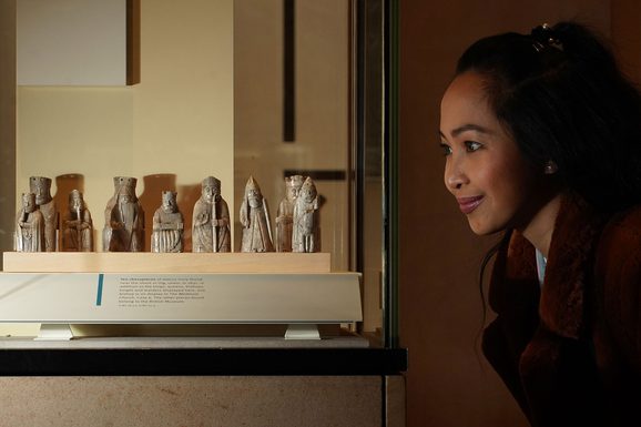 A visitor looks at the Lewis chess pieces in a glass case.