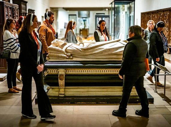 A tour group walk around the Mary Queen of Scots casket listening to an audio guide on headphones.