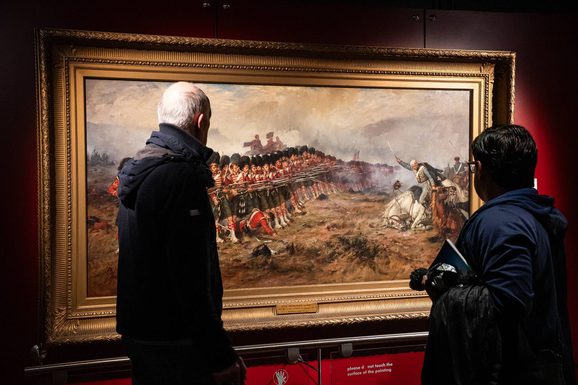 Two visitors stand looking at a painting of a battle scene