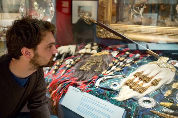 A man looking at different items of traditional Scottish dress, including kilts and sporans.