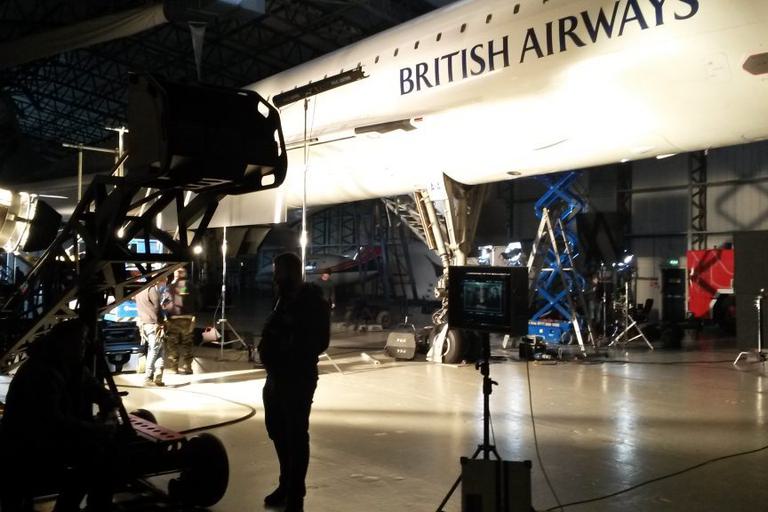 The silhouette of a film crew and equipment back lit under the Concorde jet.
