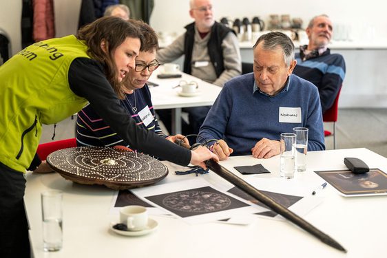 Three people gather round a table and look at a sword and shield.