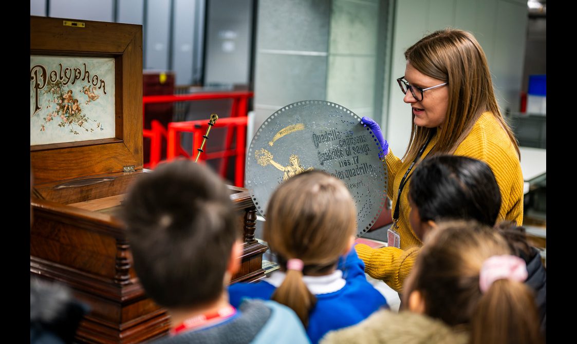 A curator from the museum shows a group of children an early version of a record player.