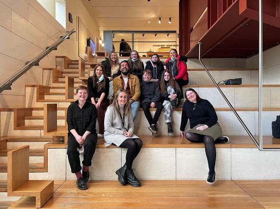 A group of people sitting on different levels of wooden steps in a museum gallery.