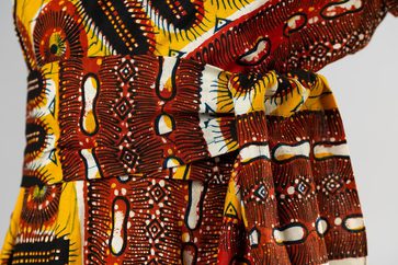 Part of a colourful wax print sundress, with patterns in reds, oranges, yellows, black, and white.