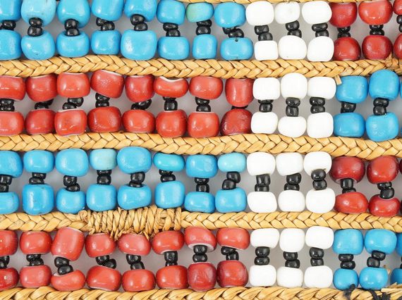 close-up of beadwork with a pattern of red and blue horizontal stripes and one white vertical crossing them all.