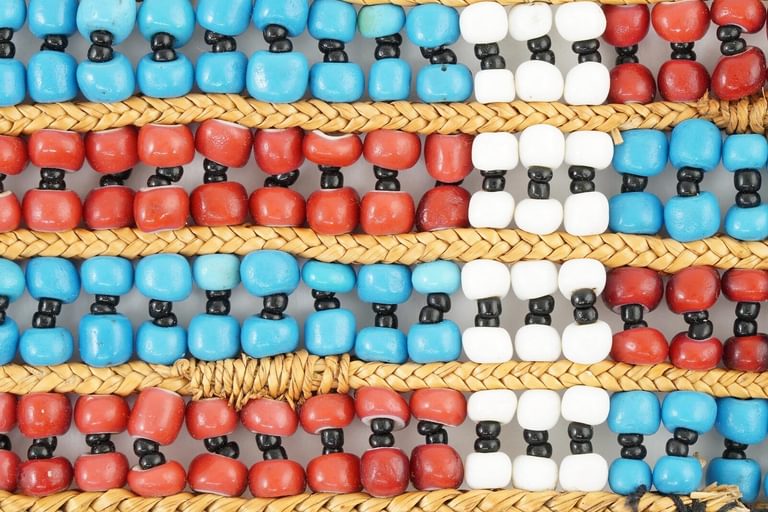 close-up of beadwork with a pattern of red and blue horizontal stripes and one white vertical crossing them all.