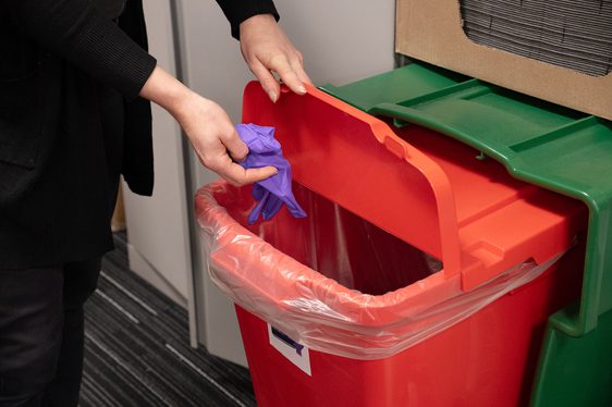 A conservator putting a pair of nitrile gloves into a red recycling box.
