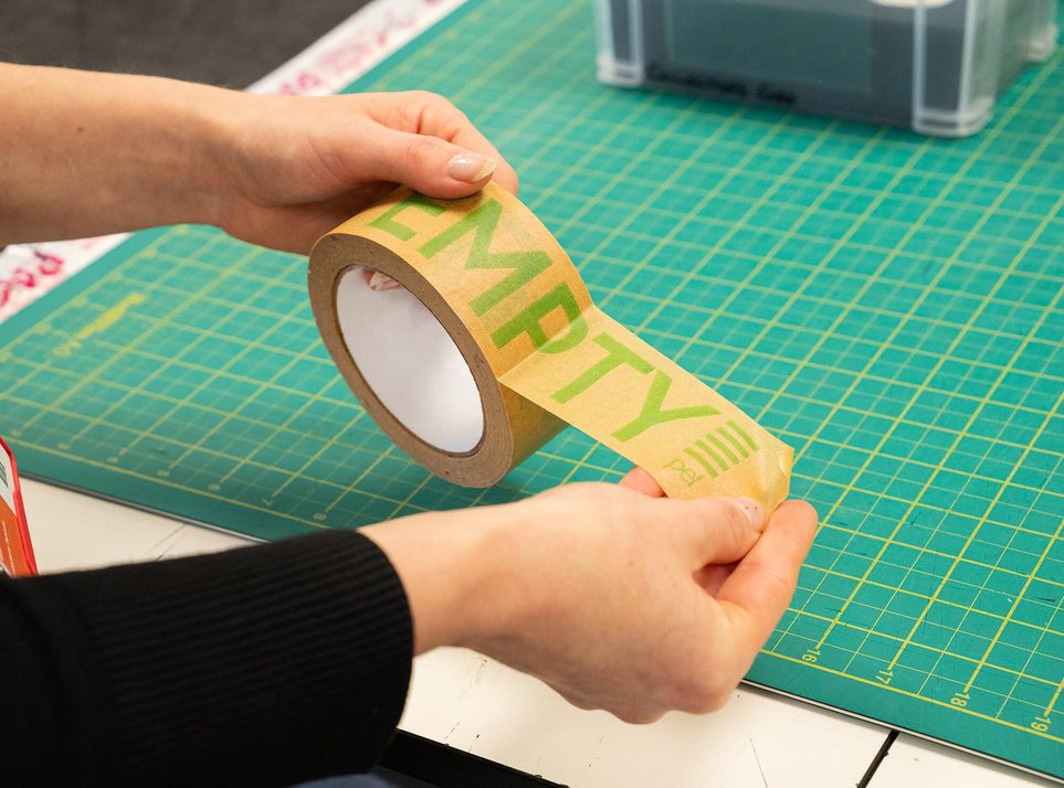 A pair of hands opening a roll of brown packing tape.