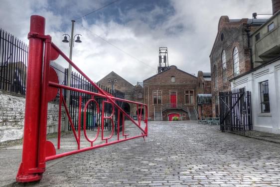 A red iron gate opening into a courtyard surrounded by old brick buildings.