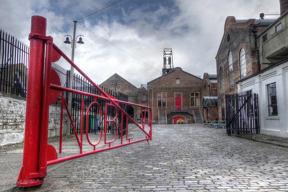 A red iron gate opening into a courtyard surrounded by old brick buildings.