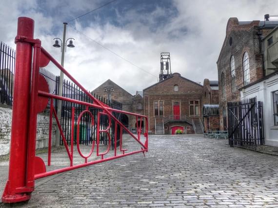 A red iron gate opening into a courtyard surrounded by old brick buildings.