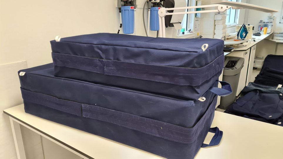 Two rectangular storage boxes covered in blue fabric made from recycled sails.