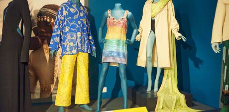 Three styled mannequins within the exhibition pose in garments of a variety of yellow and blue colours.