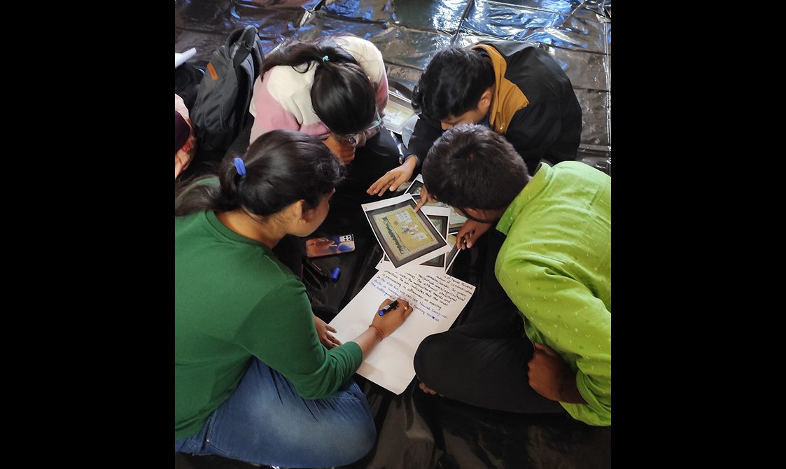 A group of students sitting on the ground, comparing images of paintings and taking notes.