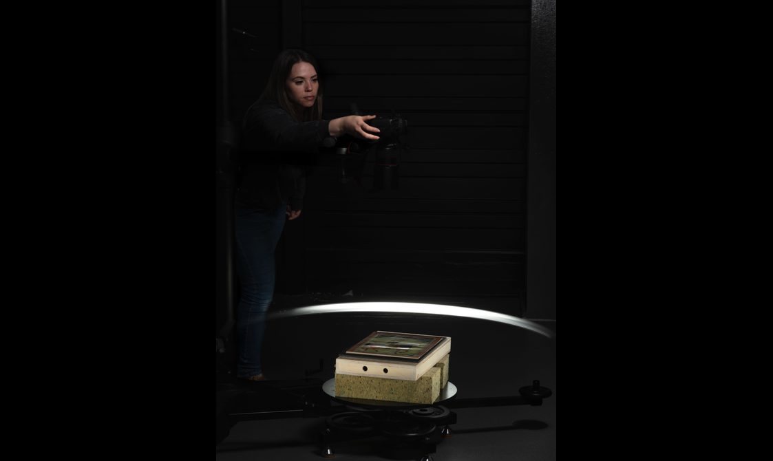 A person in a dark room with a DSLR camera above a painting.