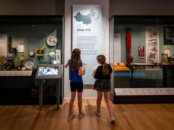 Two children read an information panel about objects from China in a museum gallery.
