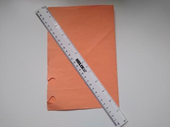 An orange paper folded in half, lying on a flat surface with a transparent long ruler placed across it.