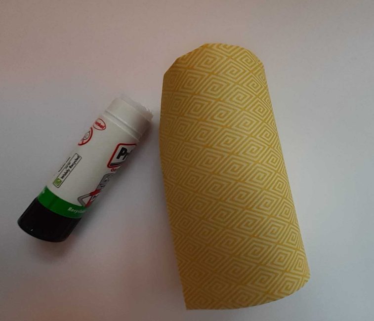 A glue stick next to a toilet roll tube covered in patterned paper.