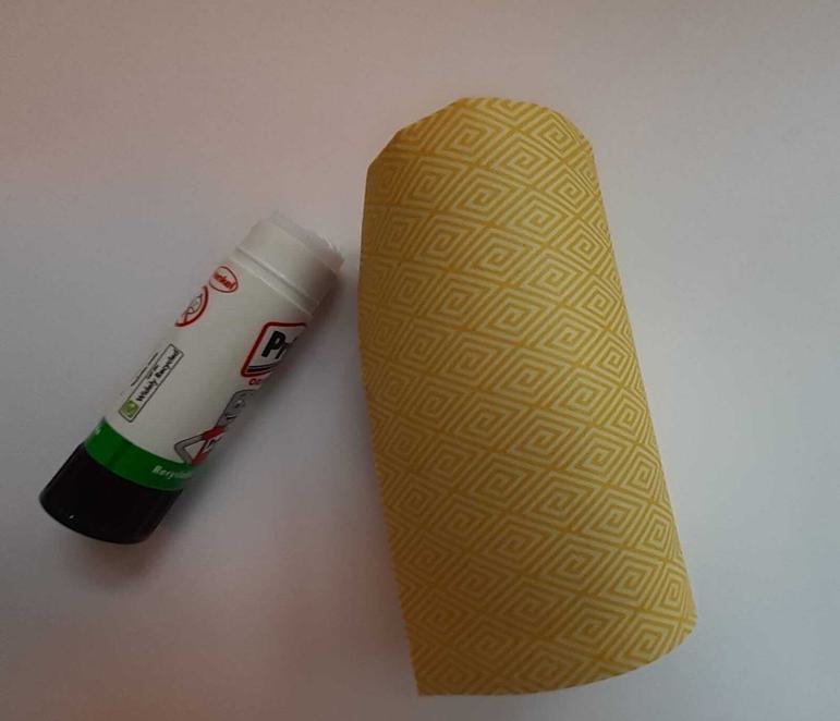 A glue stick next to a toilet roll tube covered in patterned paper.