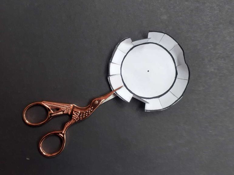 Scissors cutting petals along the edge of a paper circle.