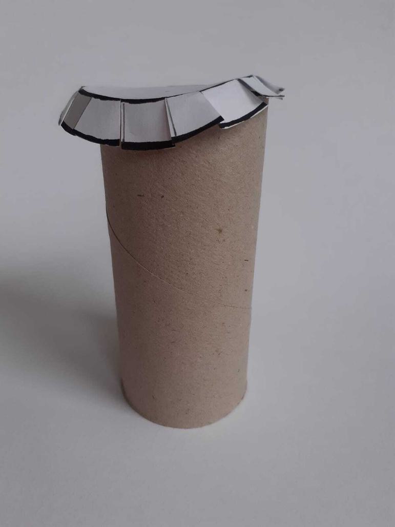 A circle with cut-out petals placed on top of a cardboard toilet roll tube.