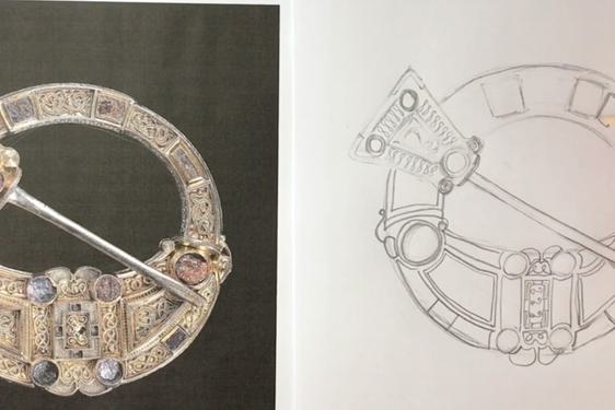 A hand holding a pencil, sketching the Hunterston brooch.