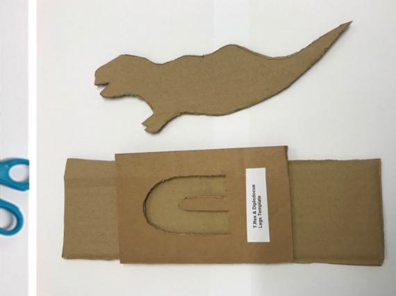 Three stages of making a cardboard dinoasaur, from drawing the outline on card to cutting it out.