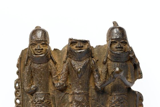 Bronze pendant chipped around the edges. Three figures in armour and heavy helmets stand side by side. The top of the middle figure's head is broken off.