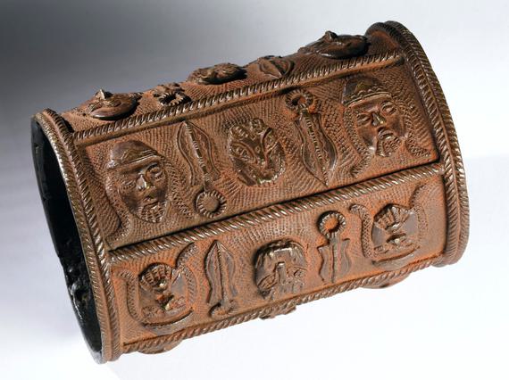 Brown-orange bronze armlet, shaped like a tube, decorated with bold symbols in relief.