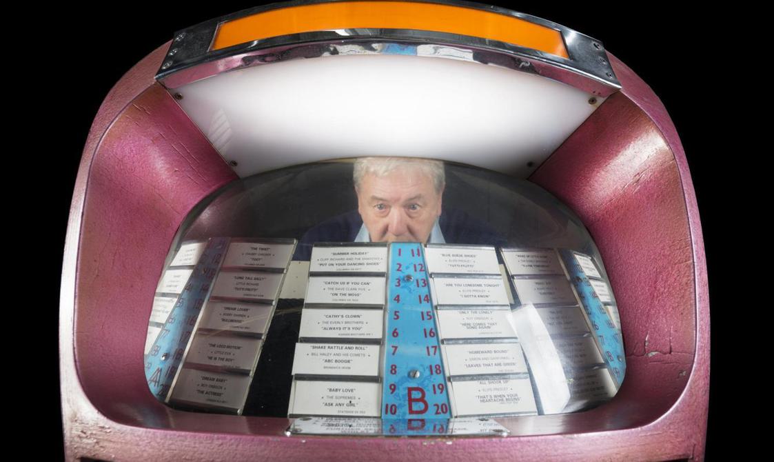 A man looking through the window of a jukebox.